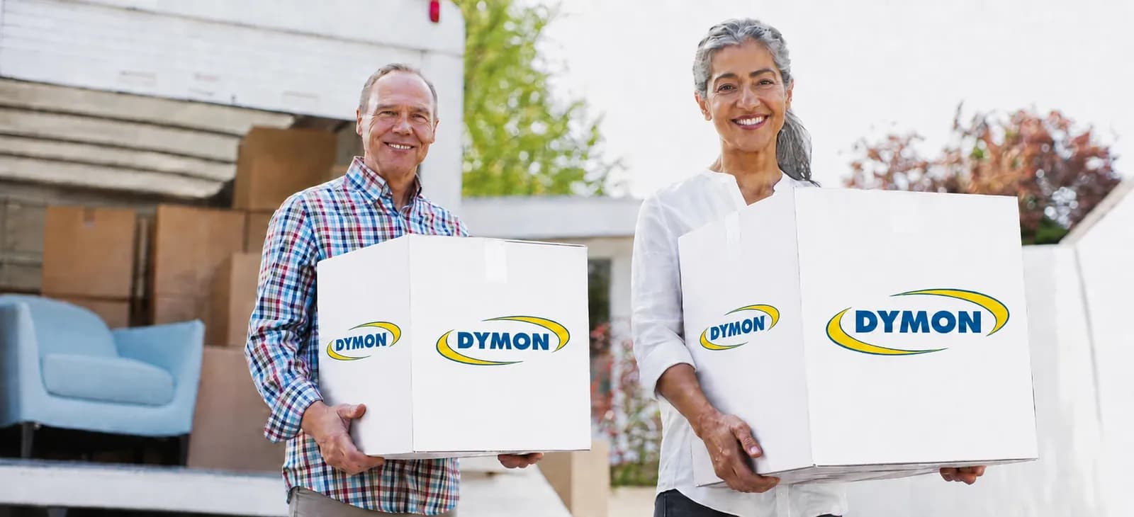Two people carrying DYMON boxes from a moving truck